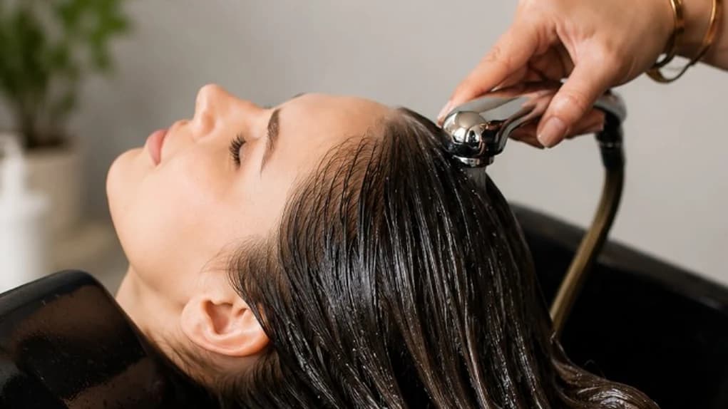 Gold hairdressing scissors and a wooden comb on a warm beige marble counter beside a folded towel — Salon at The Wellness Ed.